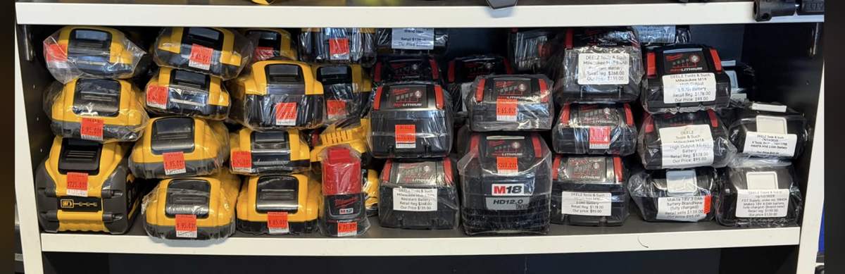 Shelf of new and used Milwaukee M18, DeWalt and Makita batteries with retail and Deelz prices marked, Calgary